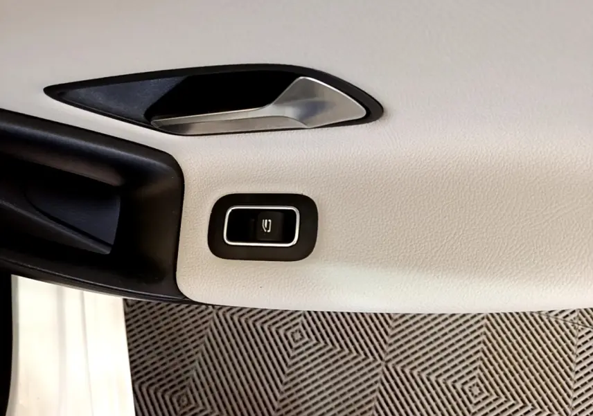 Détail de la poignée intérieure et bouton de lève-vitre sur la porte côté gauche d'une Mercedes Classe A blanche.