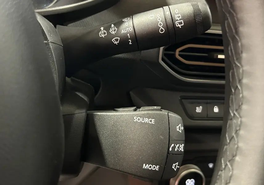 Gros plan sur la commande au volant du Dacia Jogger 2026, avec boutons source et mode, volant cuir noir visible.