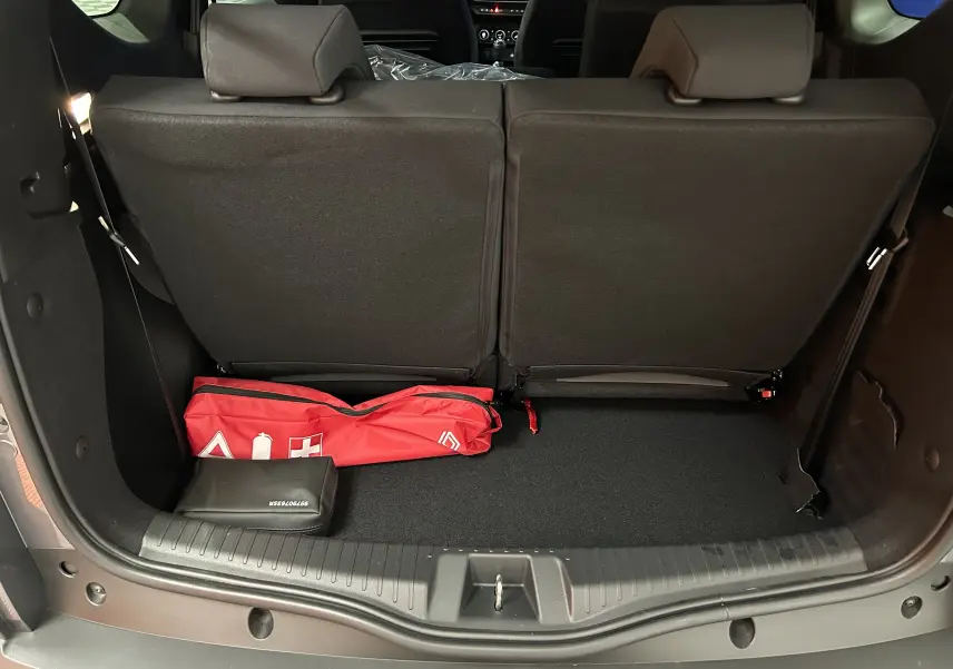 Coffre ouvert d’un Dacia Jogger gris schiste, vue arrière montrant la banquette arrière et un kit de sécurité rouge.