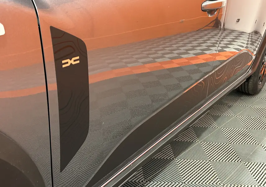 Gros plan sur la porte côté gauche du Dacia Jogger gris schiste métal avec décor noir et logo distinctif.