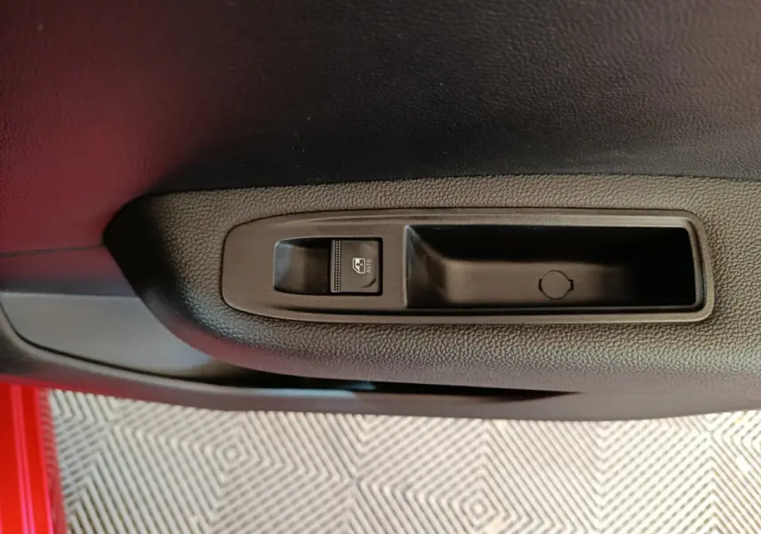 Gros plan sur le bouton de commande de la vitre électrique côté conducteur d'une Renault Clio rouge 2024.