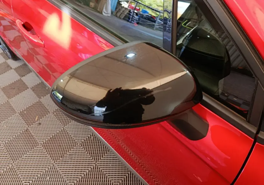 Rétroviseur noir en gros plan côté gauche d’une Renault Clio rouge 2024, avec porte et vitre partiellement visibles.