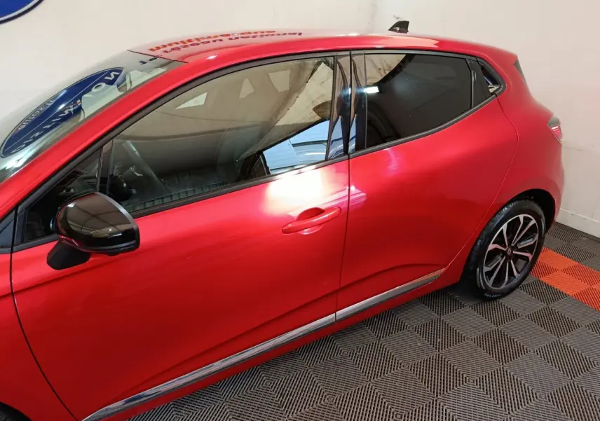 Profil droit d'une Renault Clio rouge 2024 avec rétroviseur noir brillant et jantes alliage distinctives.