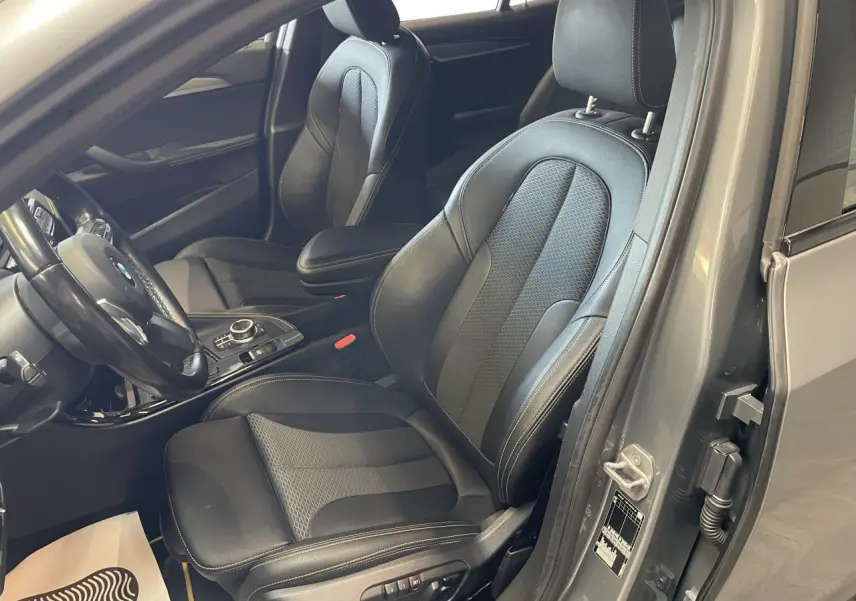 Vue intérieure côté conducteur d'une BMW X2 M Sport X 2022 gris foncé avec sièges en similicuir noir et surpiqûres contrastantes.