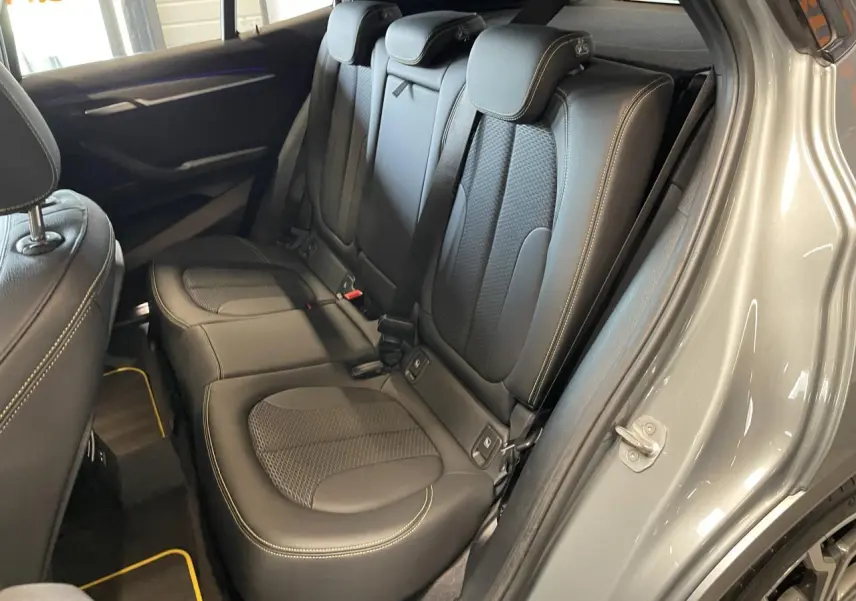 Vue intérieure côté arrière droit du BMW X2 M Sport X gris foncé, montrant les sièges en similicuir noir avec surpiqûres jaunes.