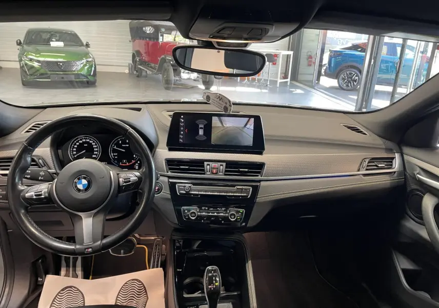 Vue intérieure avant du tableau de bord gris anthracite du BMW X2 M Sport X avec volant M cuir et écran central tactile.