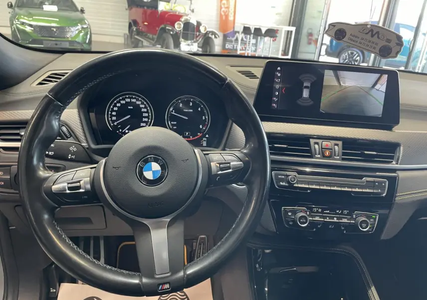 Vue intérieure centrée sur le volant cuir M et le tableau de bord avec écran multimédia du BMW X2 gris foncé.
