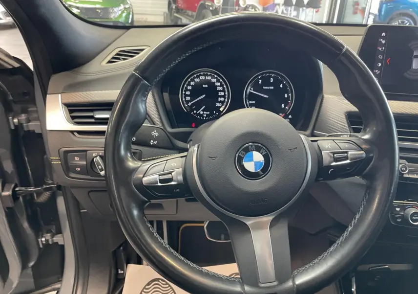 Vue intérieure centrée sur le volant M cuir noir et le tableau de bord du BMW X2 gris foncé 2022.
