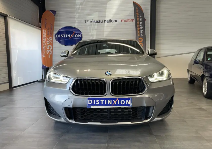 Vue frontale d'une BMW X2 M Sport X gris foncé avec phares LED allumés en intérieur showroom.