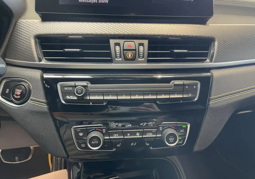 Vue rapprochée du tableau de bord de la BMW X2 M Sport X 2022, montrant la console centrale avec commandes climatisation et bouton Start/Stop.
