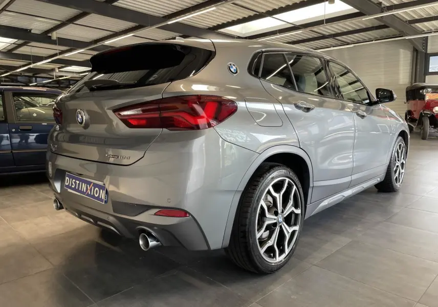 BMW X2 sDrive 18d gris foncé vue 3/4 arrière droit avec jantes 19 pouces style 722 M et double sortie d’échappement chromée.