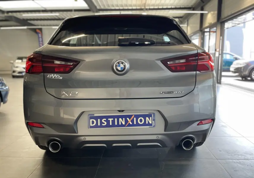 Vue arrière d'une BMW X2 sDrive18d gris foncé avec double sortie d'échappement chromée en intérieur showroom.