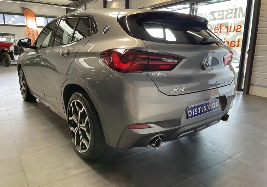 BMW X2 sDrive 18d gris foncé vue 3/4 arrière droit, avec jantes alliage 19" style 722 M et double sortie d’échappement chromée.