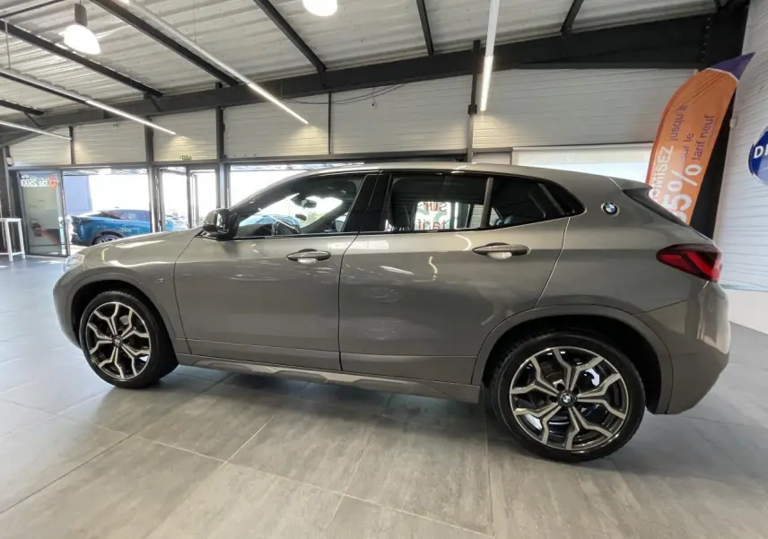 BMW X2 sDrive 18d M Sport X gris foncé vue de profil côté gauche avec jantes alliage 19 pouces style 722 M en showroom.