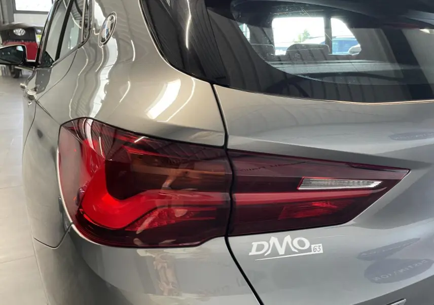 Gros plan sur le feu arrière gauche d’une BMW X2 gris foncé, mettant en valeur la finition M Sport X et le logo DMO.