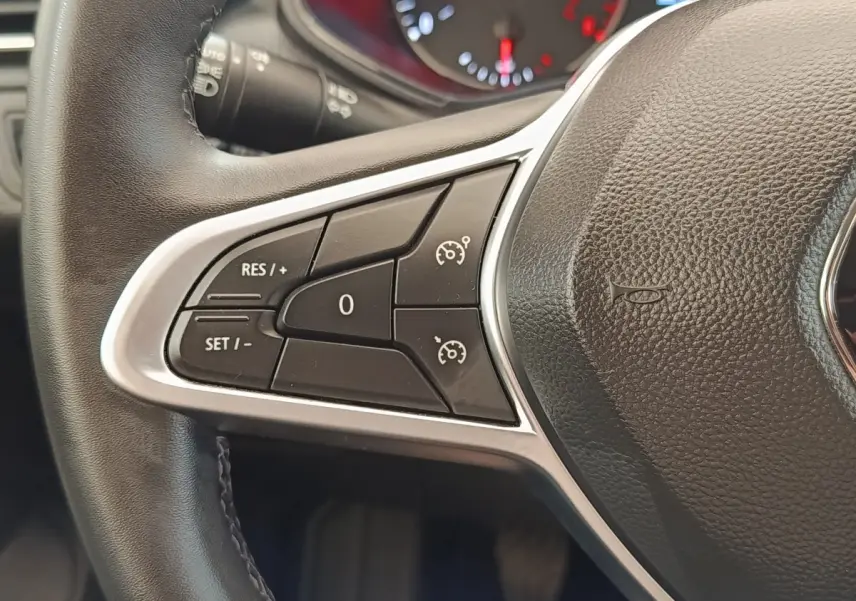 Gros plan sur la partie gauche du volant cuir noir de la Renault Clio blanc, avec commandes de régulateur de vitesse.