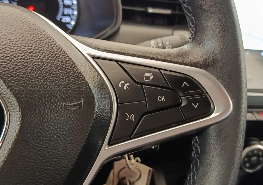 Gros plan sur les commandes multifonctions noires du volant en cuir noir de la Renault Clio Business blanche.