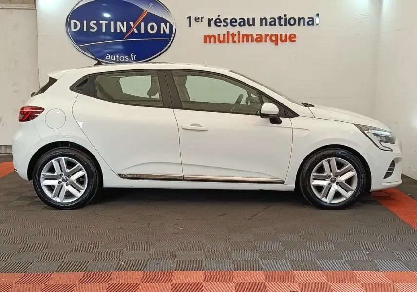 Profil droit d'une Renault Clio Business TCe 100 GPL blanche 2021 avec jantes alliage et logo Distinxion en arrière-plan.