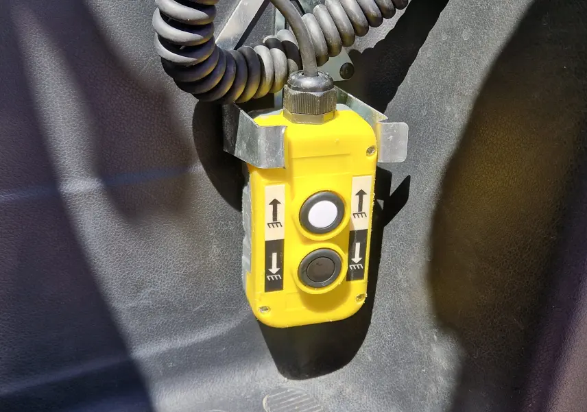 Gros plan sur la télécommande jaune de la benne du Renault Master blanc, avec deux boutons pour lever et baisser la benne.