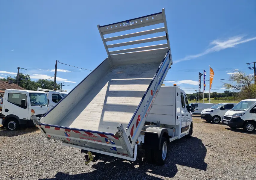 Renault Master Chassis double cabine blanc vu 3/4 arrière avec benne relevée et coffre latéral sur terrain extérieur.