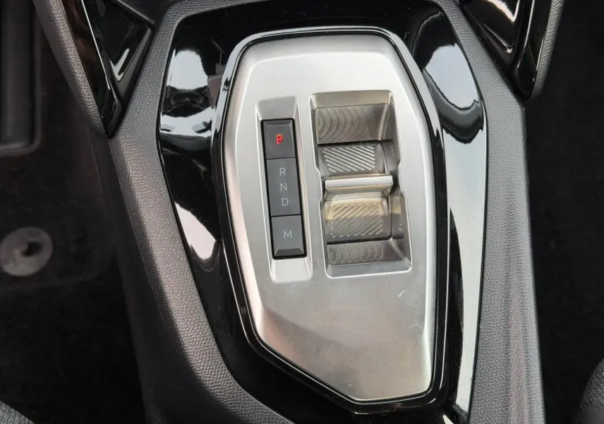 Gros plan sur la console centrale noire et argentée de la Peugeot 208 Hybrid, avec levier de vitesses automatique.