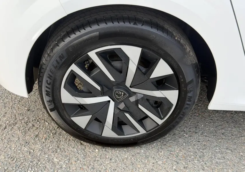 Gros plan sur la roue avant droite d'une Peugeot 208 blanche avec jante alliage au design géométrique.