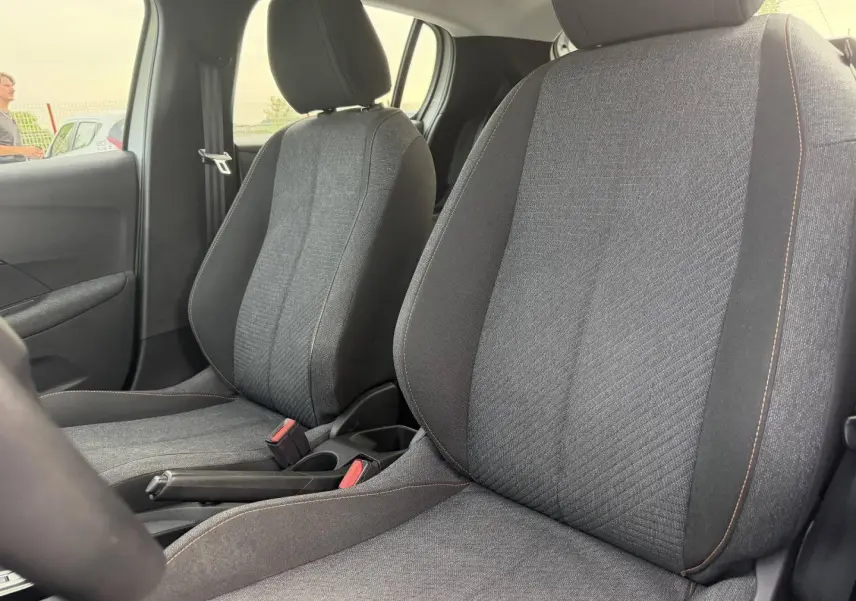 Vue rapprochée des sièges avant en tissu gris avec surpiqûres orange de la Peugeot 208 hybride blanche.