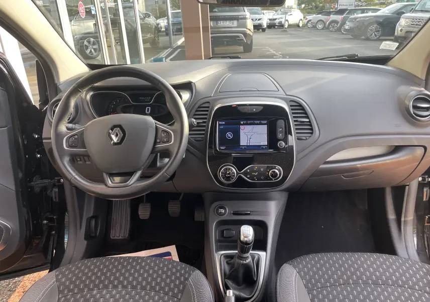 Vue intérieure frontale du tableau de bord du Renault Captur noir, avec volant multifonction et écran GPS tactile central.