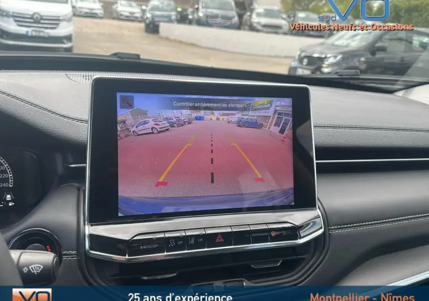 Vue intérieure sur l'écran tactile affichant la caméra de recul du Jeep Compass bleu, avec tableau de bord noir et commandes visibles.