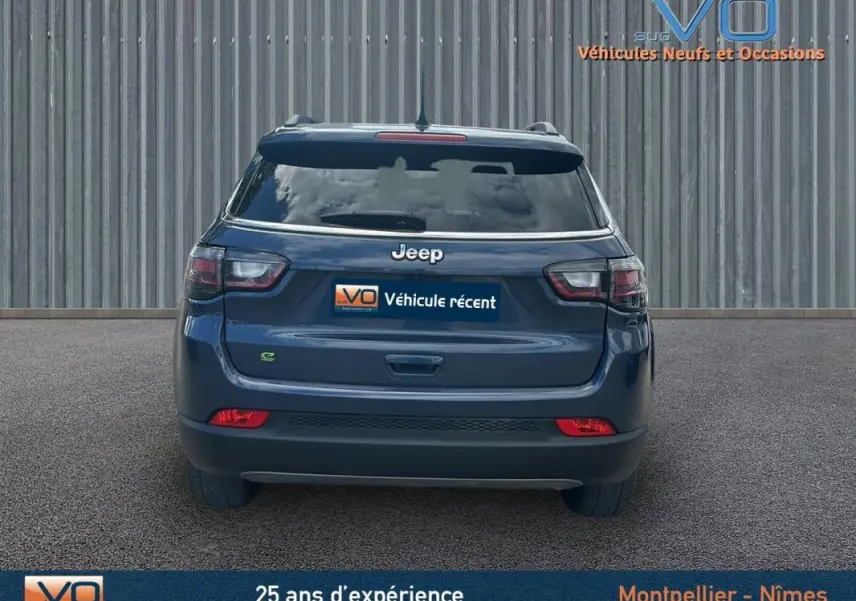 Vue arrière d'un Jeep Compass bleu 2023 avec barres de toit et feux arrière LED visibles sur sol goudronné.