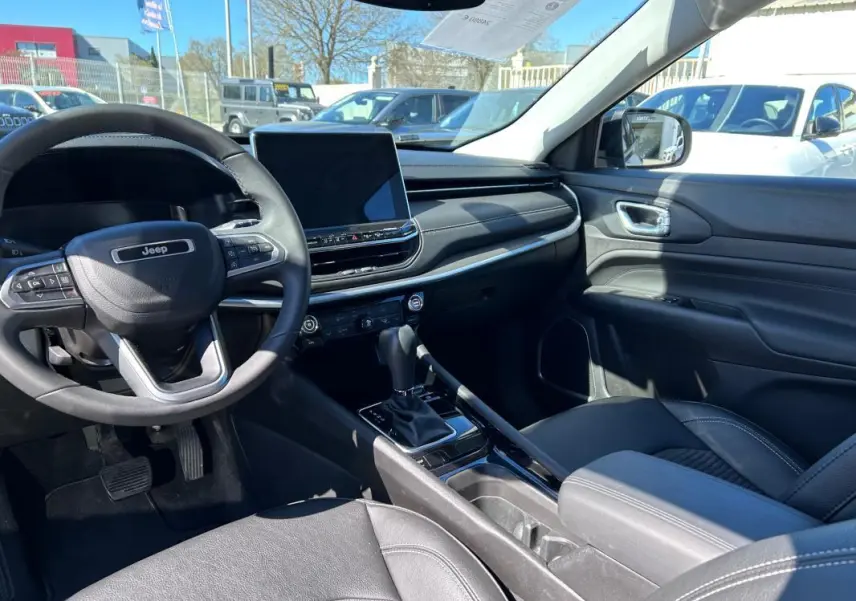 Vue intérieure côté conducteur du Jeep Compass 2024 gris, montrant volant, écran tactile et accoudoir central.