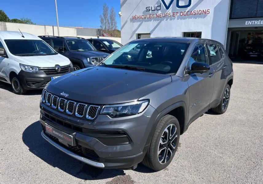 Jeep Compass gris en 3/4 avant droit, avec jantes alliage 18 pouces et calandre chromée, stationné devant un concessionnaire.