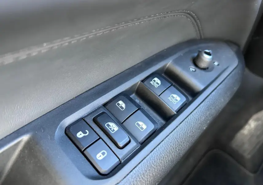 Gros plan sur les commandes de lève-vitres et rétroviseurs sur la porte côté conducteur du Jeep Compass gris 2024.