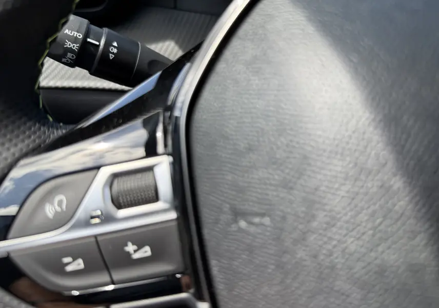 Gros plan sur le volant noir en cuir du Peugeot 2008 Hybrid 145ch, avec commandes intégrées et levier de clignotant visible.