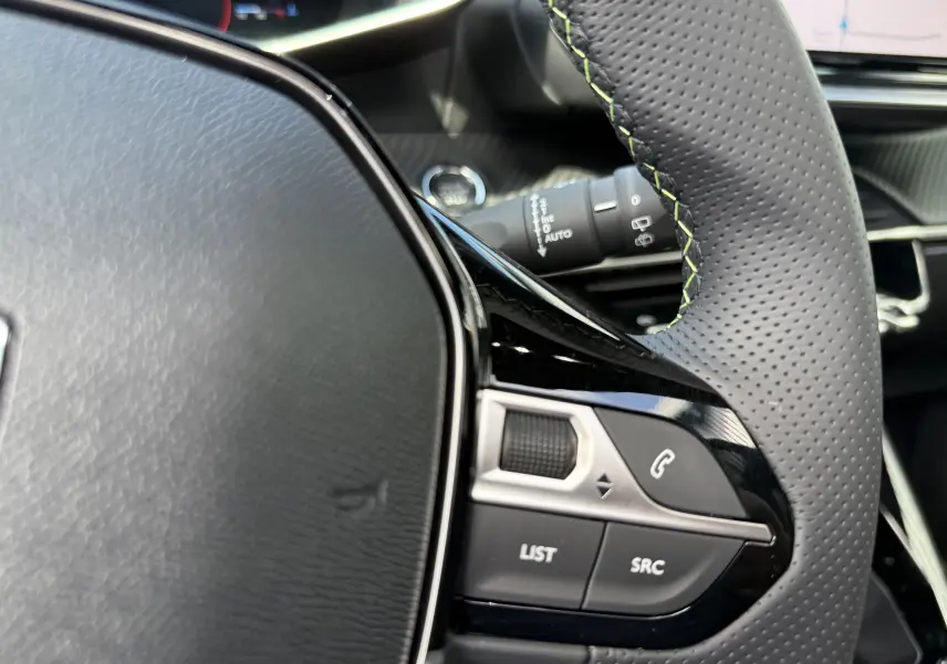 Détail du volant perforé avec surpiqûres vertes du Peugeot 2008 Hybrid 145ch GT, boutons de commande intégrés.