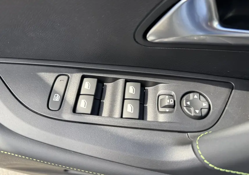 Détail des commandes des vitres et rétroviseurs côté conducteur du Peugeot 2008 gris avec surpiqûres vertes.