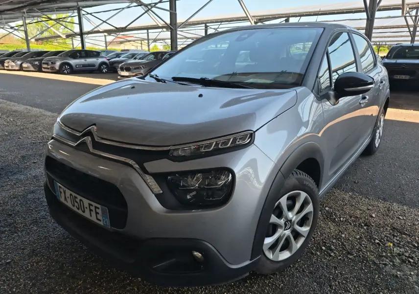 Citroën C3 gris Artense vue 3/4 avant droit, avec phares distinctifs et calandre chromée sous abri.