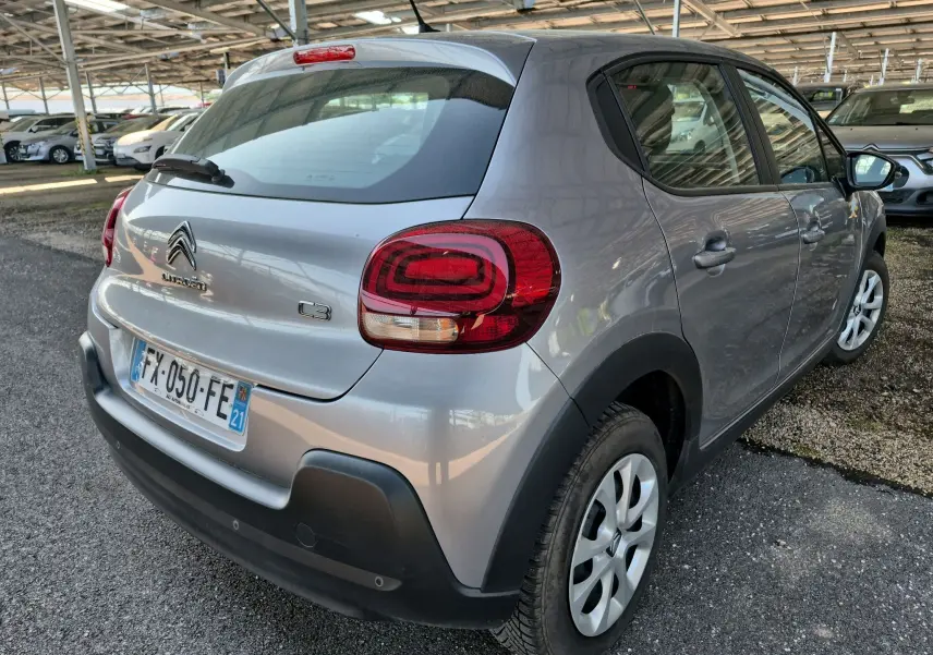 Vue 3/4 arrière droite d'une Citroën C3 gris Artense 2021 avec feux arrière rouges et jantes blanches.