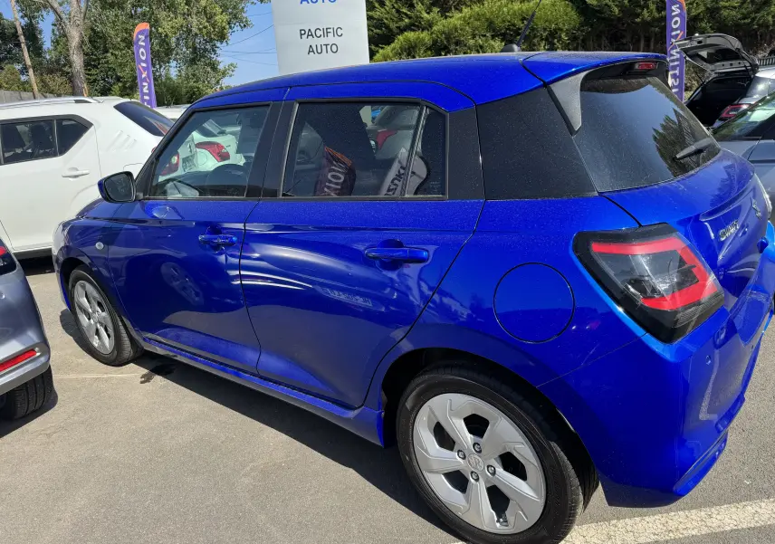 Vue 3/4 arrière droite d'une Suzuki Swift 1.2 Privilège Hybrid bleue, avec hayon et feux arrière distinctifs.