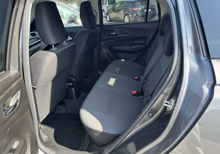 Vue intérieure côté arrière droit de la Suzuki Swift 1.2 Privilège Hybrid 2025, sièges tissu gris et portes ouvertes.