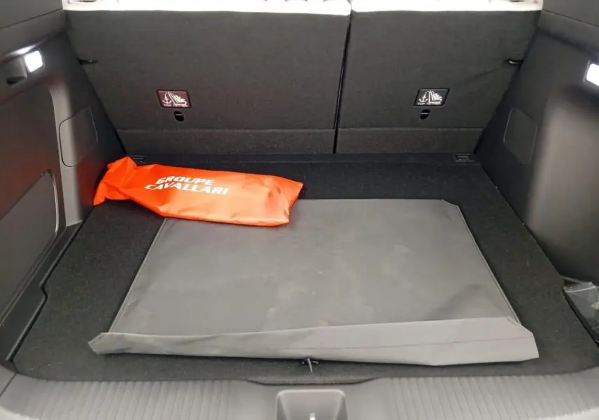 Coffre ouvert du Honda e:Ny1 204 ch Advance 2025, vue intérieure montrant un tapis noir et une trousse orange.
