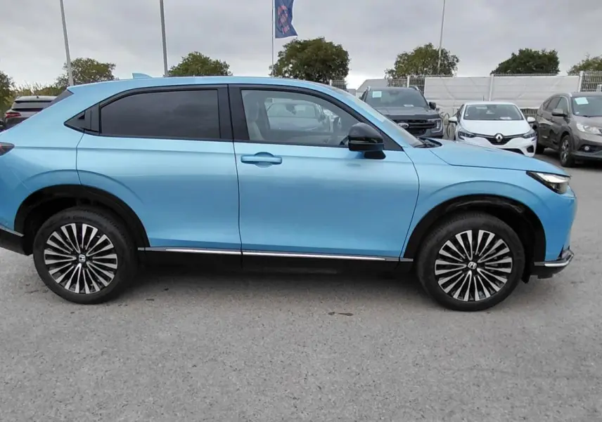 Vue de profil côté gauche du SUV électrique Honda e:Ny1 204 ch Advance bleu 2025 avec jantes distinctives bicolores.