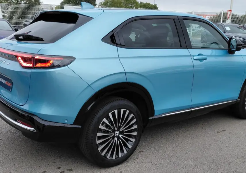 Vue 3/4 arrière droite d'un Honda e:Ny1 bleu électrique 2025 avec feux arrière LED et jantes distinctives.