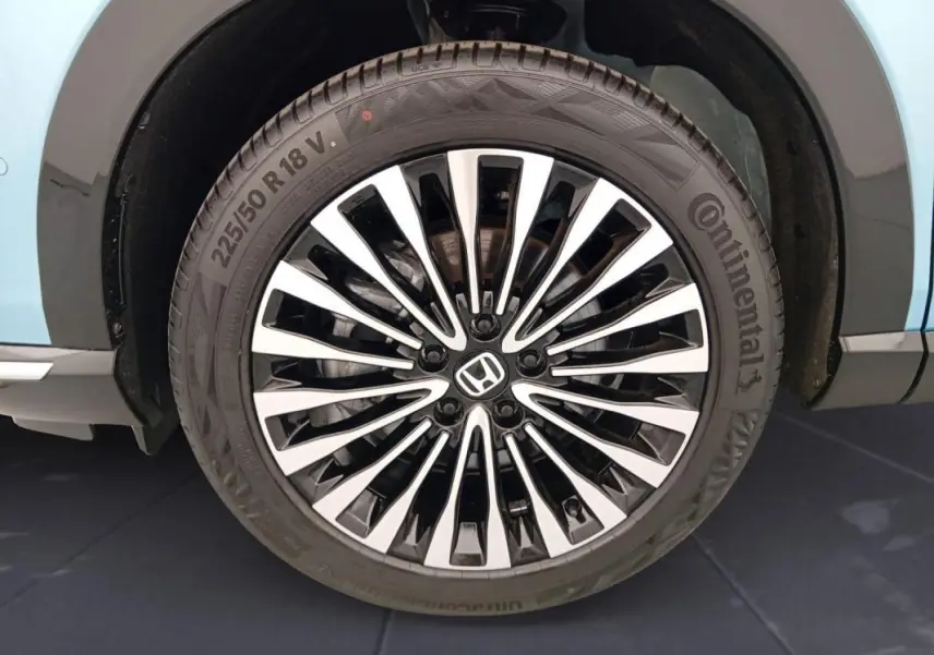 Gros plan sur la roue avant droite bleu clair du Honda e:Ny1 204 ch Advance 2025 avec jante alliage noire et argentée.