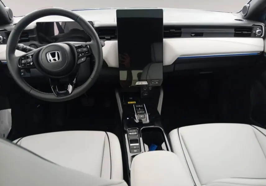 Vue intérieure avant du Honda e:Ny1 204 ch Advance 2025, tableau de bord blanc avec écran tactile vertical et volant noir.