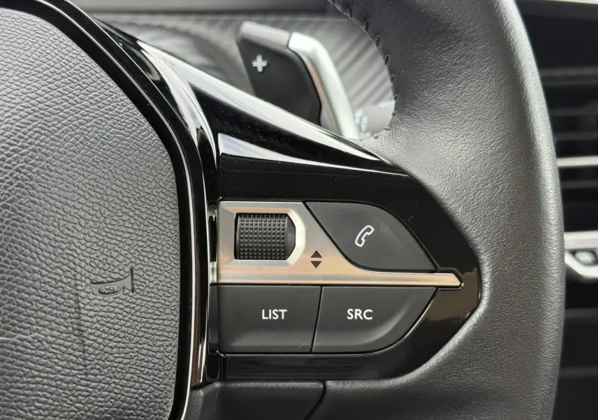 Gros plan sur les commandes noires et argentées au volant du Peugeot 208 noir Perla Nera, avec molette et boutons d’appel.