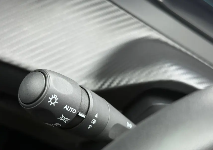 Gros plan sur la commande des phares automatique dans l’habitacle noir de la Peugeot 208 1.2 Hybrid 2025.
