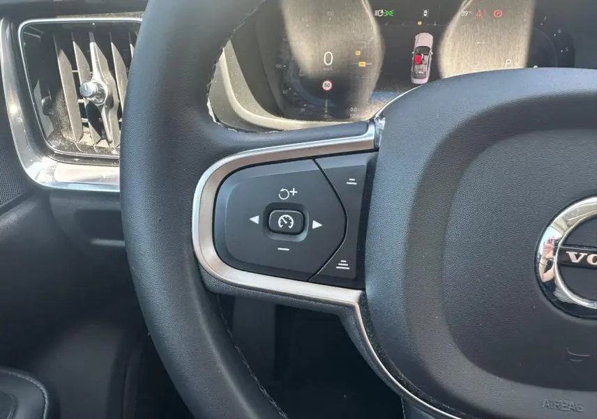 Gros plan sur le volant noir et les commandes de régulateur de vitesse du Volvo S60 2024 en Thunder Grey Metal.
