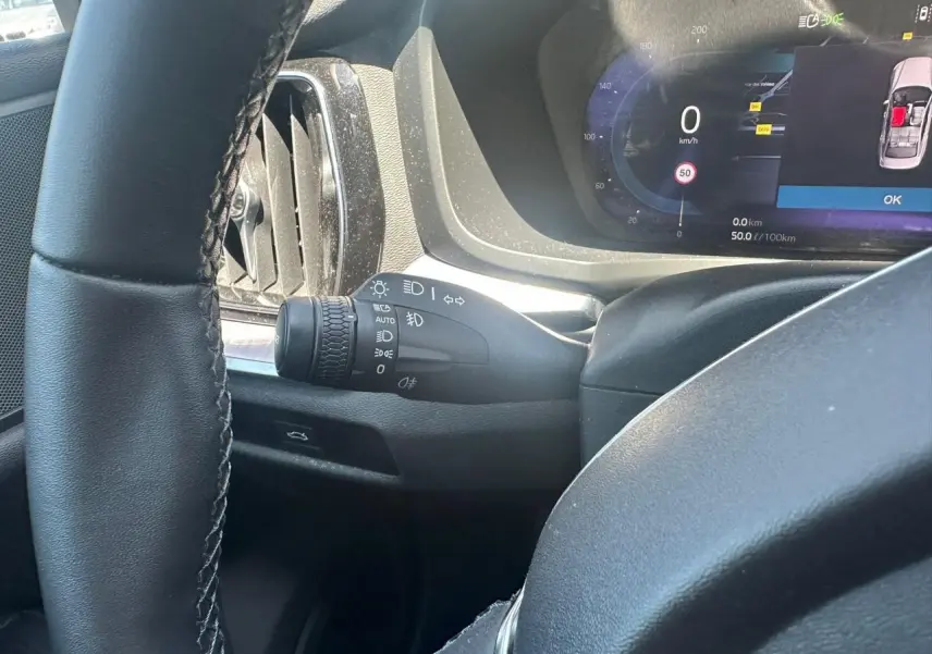 Vue intérieure côté gauche du volant noir d'une Volvo S60 2024 avec tableau de bord digital et commandes lumineuses intégrées.