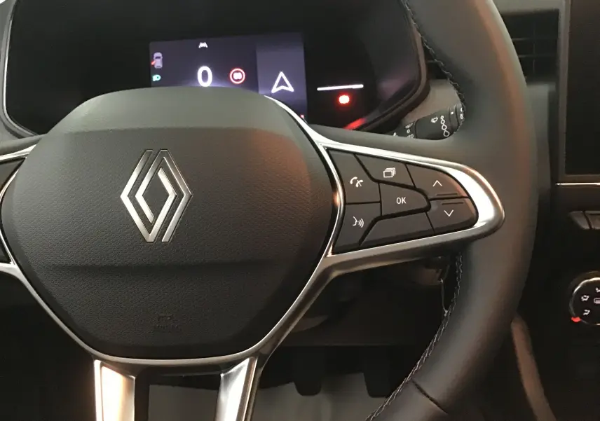 Gros plan sur le volant noir de la Renault Clio V 2025 avec commandes intégrées et affichage numérique en arrière-plan.